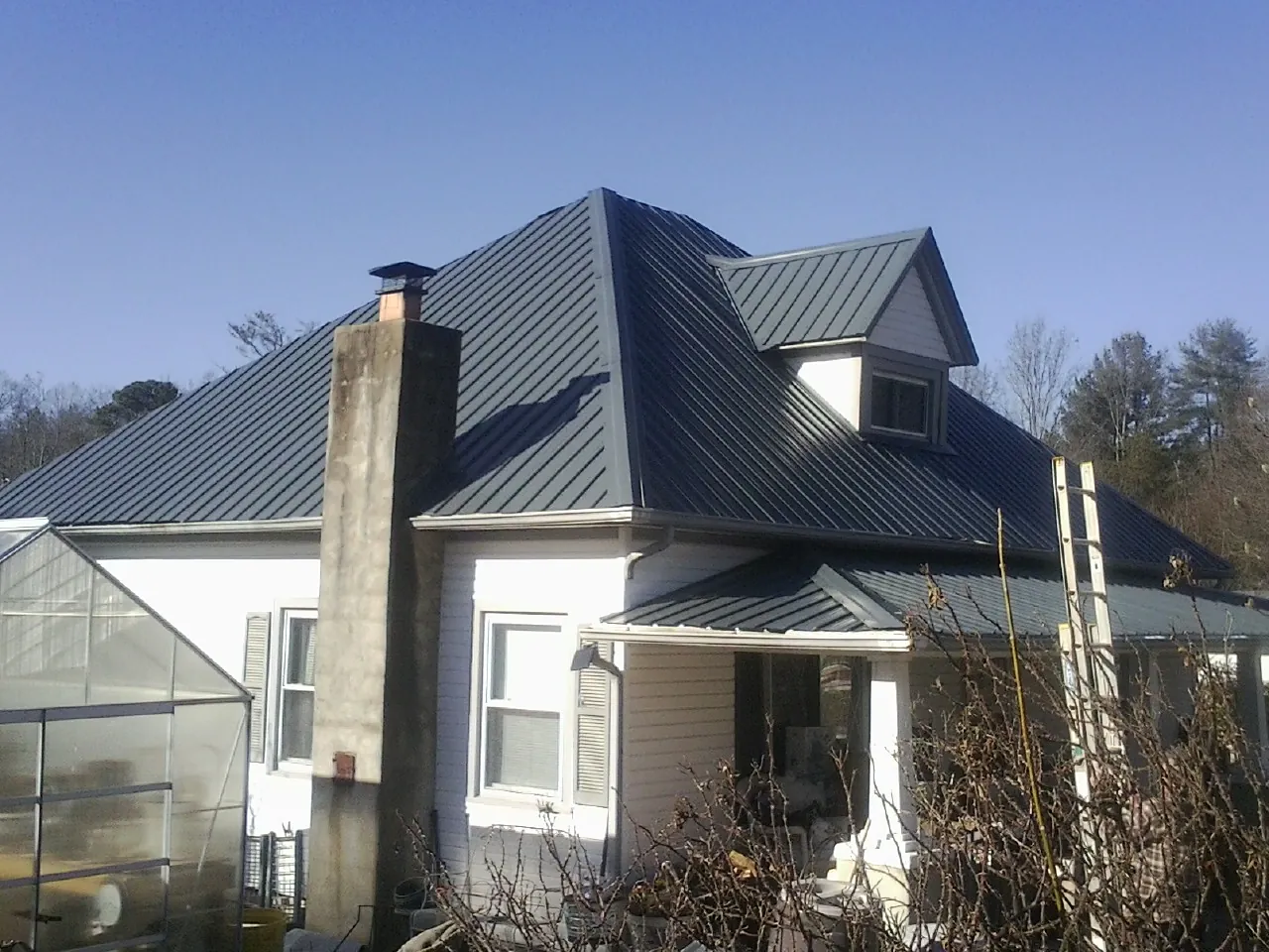 Dark blue standing seam metal roof on a white farmhouse with dormer — Slate & Tile Roof Repair by Roofing Brothers in Campton