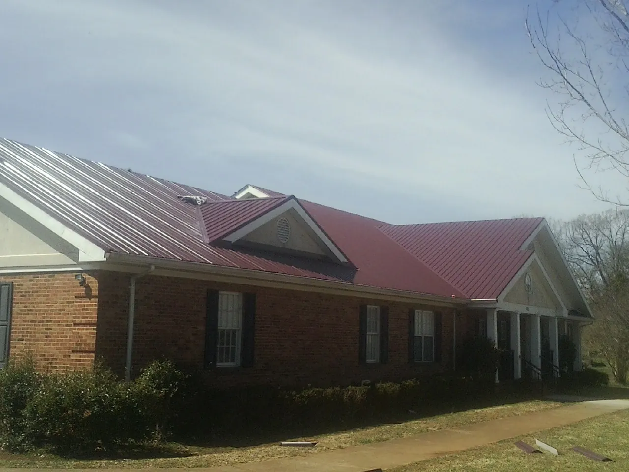 Red metal roof with gabled entries on a long brick building, from a Hail Damage Roof Repair job in Campton
