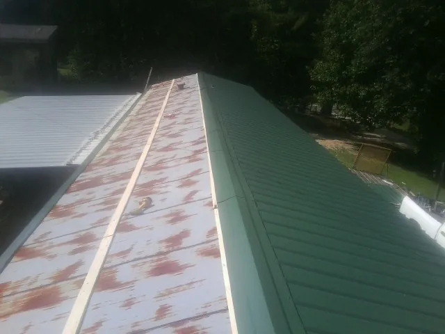 Old rusted panels beside newly installed green metal roofing — Wind Damage Roof Repair by Roofing Brothers in Campton