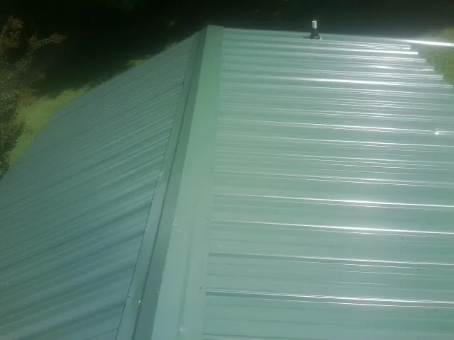 New green metal panels meeting at the ridge of a roof — Flat Roof Repair work by our crew in Campton