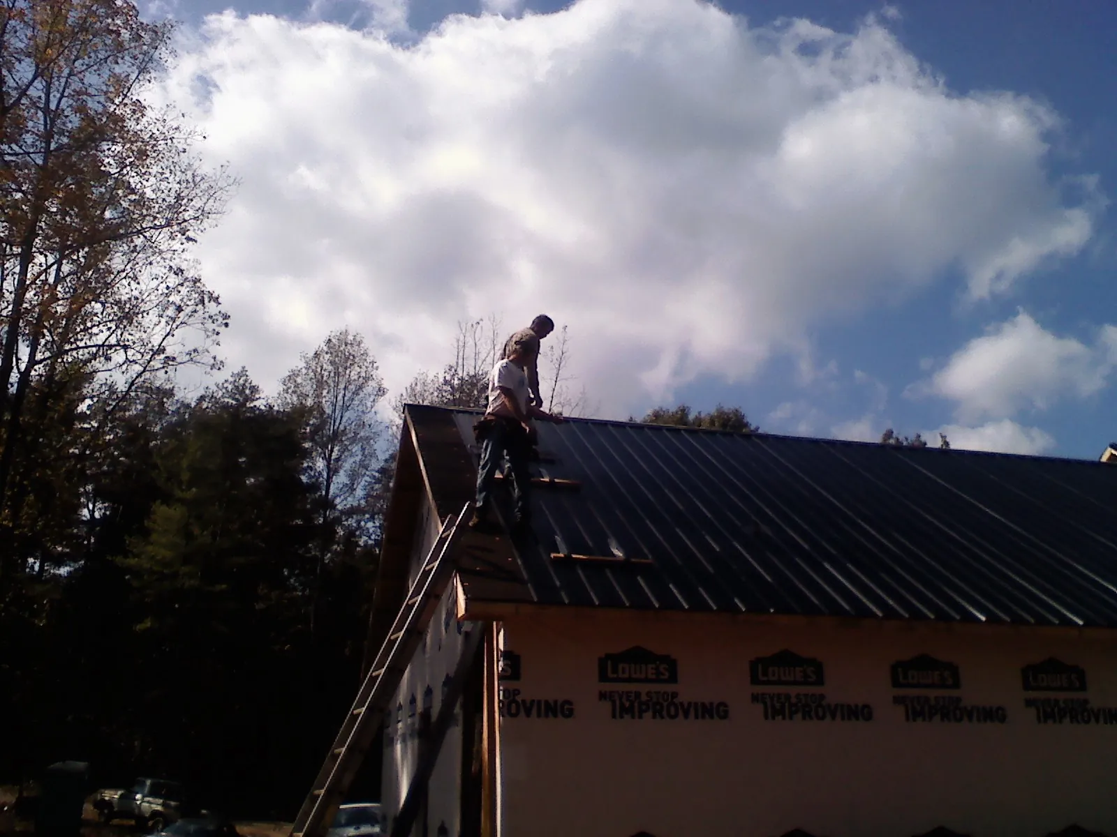 Roofer fastening dark metal panels high against a cloudy sky, from a Roof Inspection job in Campton